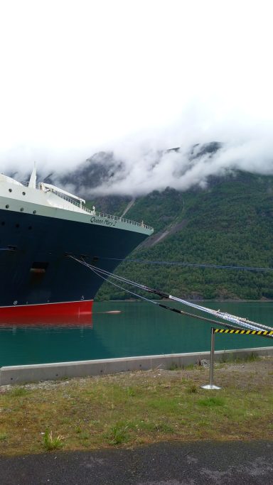 A large ship moored near a mountainous area shrouded in clouds.