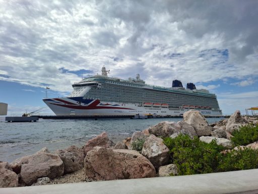 A large cruise ship docked beside stone shoreline under a cloudy sky.