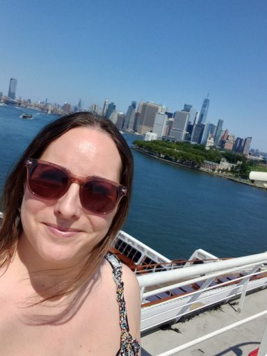Jodie in sunglasses smiles with New York city skyline and waterfront in the background.