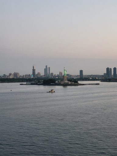 View of a city skyline with a statue on an island, reflecting in the water.