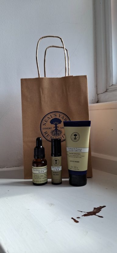Three skincare products beside a brown paper bag from Neil's Yard Remedies on a white surface.