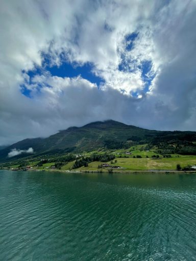 A serene landscape with a mountain, green hills, and a partially cloudy sky reflecting on water.