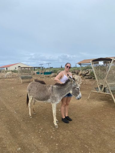 Jodie stands beside a donkey on a farm, smiling at the camera.