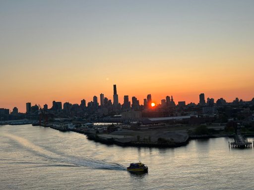 Sunset over a city skyline with a boat on the water in the foreground.