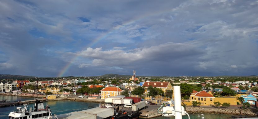 Panoramic view of a coastal town with colourful buildings and a rainbow in the sky.