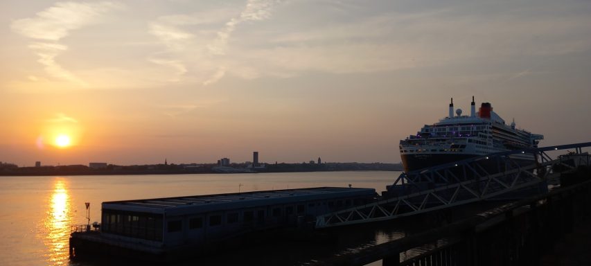 Sunset over a river with a large cruise ship docked beside a jetty.