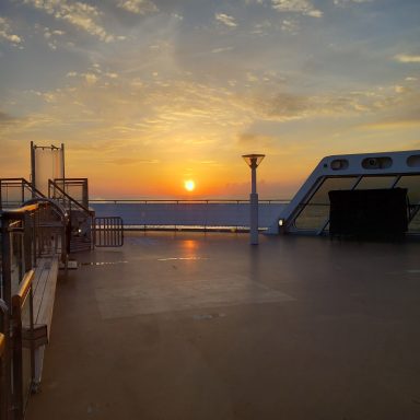 Sunset over the sea viewed from a deck, with soft clouds in the sky.