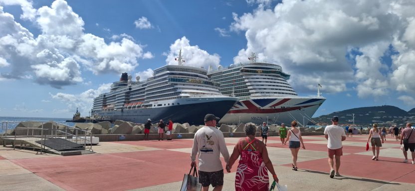 Large cruise ship docked near a waterfront promenade with people walking by.