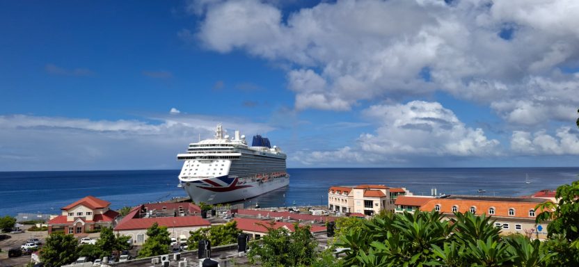 Cruise ship docked by a coastal town under a cloudy blue sky.
