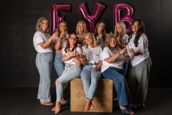 Jodie and a group of young women from the Feel Your Best community posing together with pink balloons spelling "FYB."