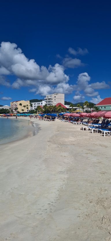 A sunny beach scene with lounge chairs, umbrellas, and a clear blue sky.