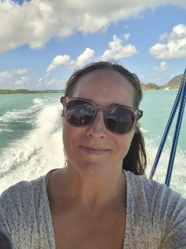Jodie smiling in sunglasses on a boat with turquoise water and clouds in the background.