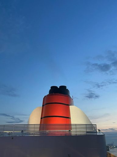 Red and white ship smokestack against a clear blue sky at twilight.